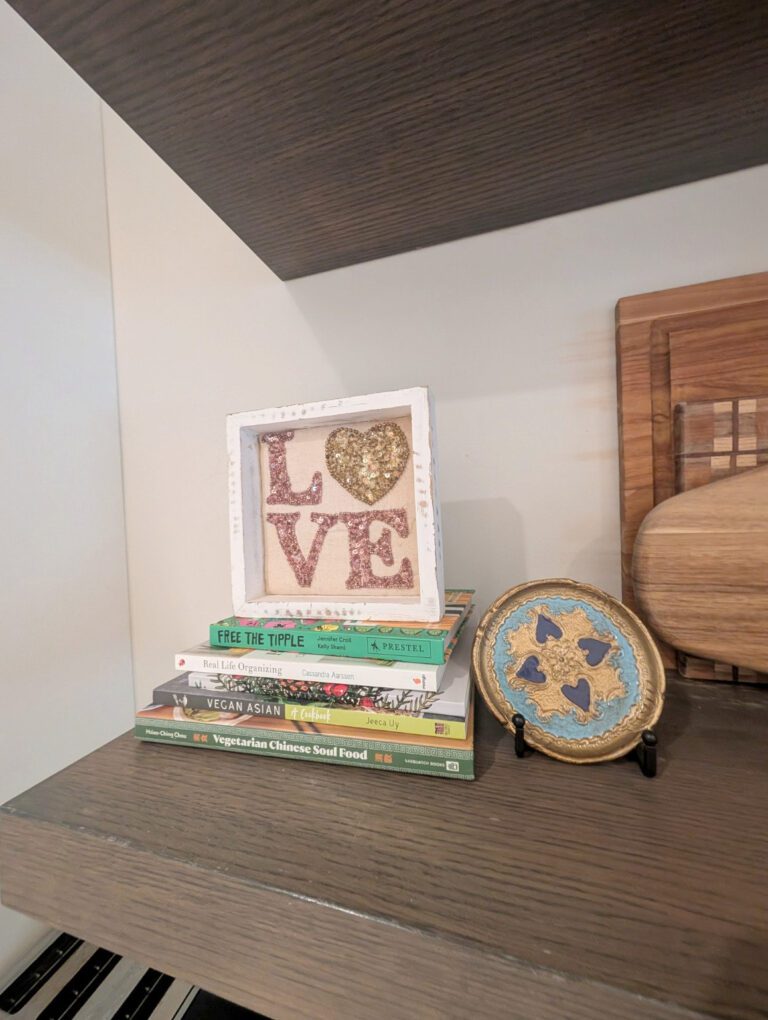 Decorative shelf vignette styled with books, a LOVE frame and an ornate plate using the client's existing belongings